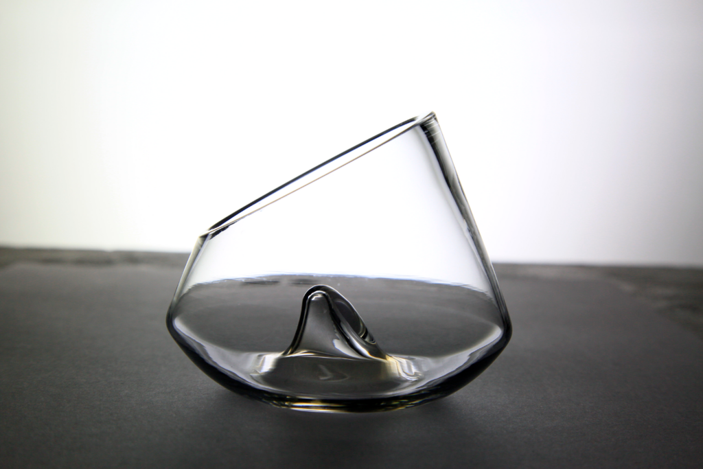 La copa cónica de cristal transparente vista desde abajo, apoyada directamente sobre una superficie oscura y mostrando el pico central en su base interior.