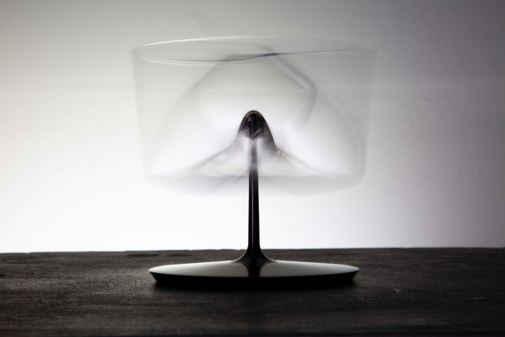 Fotografía en blanco y negro y larga exposición de la copa balanceándose sobre su pie metálico, con el cristal difuminado por el movimiento de vaivén.