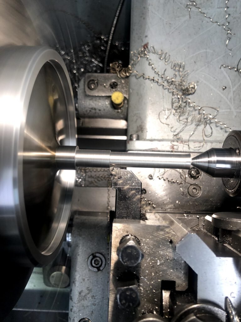 Torno de precisión mecanizando una pieza metálica cilíndrica, con virutas de metal enroscadas alrededor de la herramienta de corte.