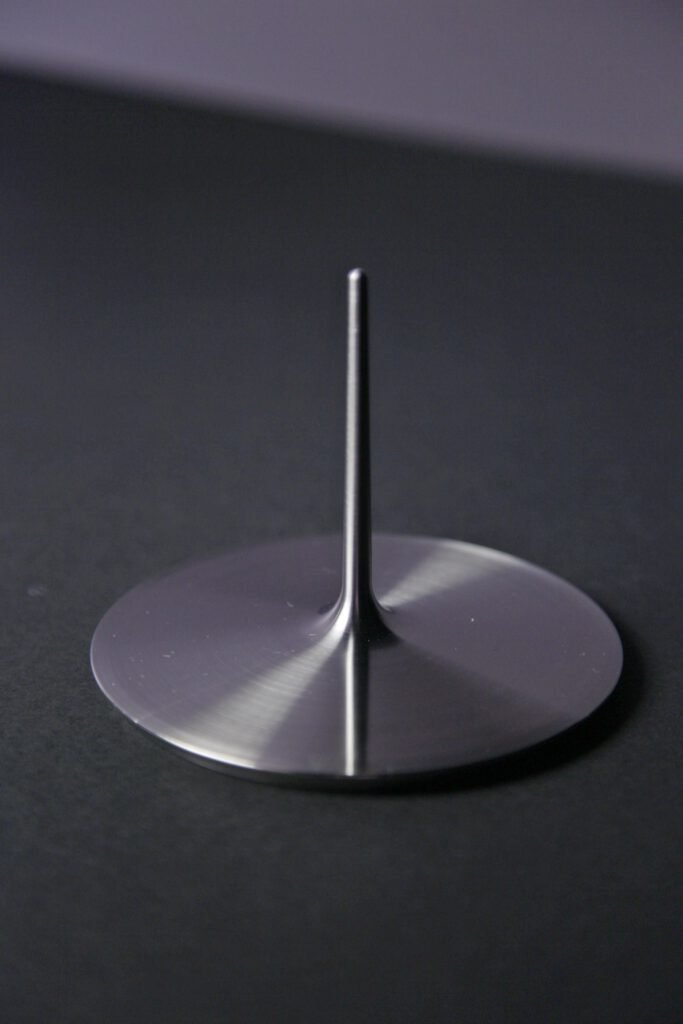 La base metálica pulida de la copa, con su fino vástago vertical y el disco circular de apoyo, fotografiada sobre un fondo oscuro.