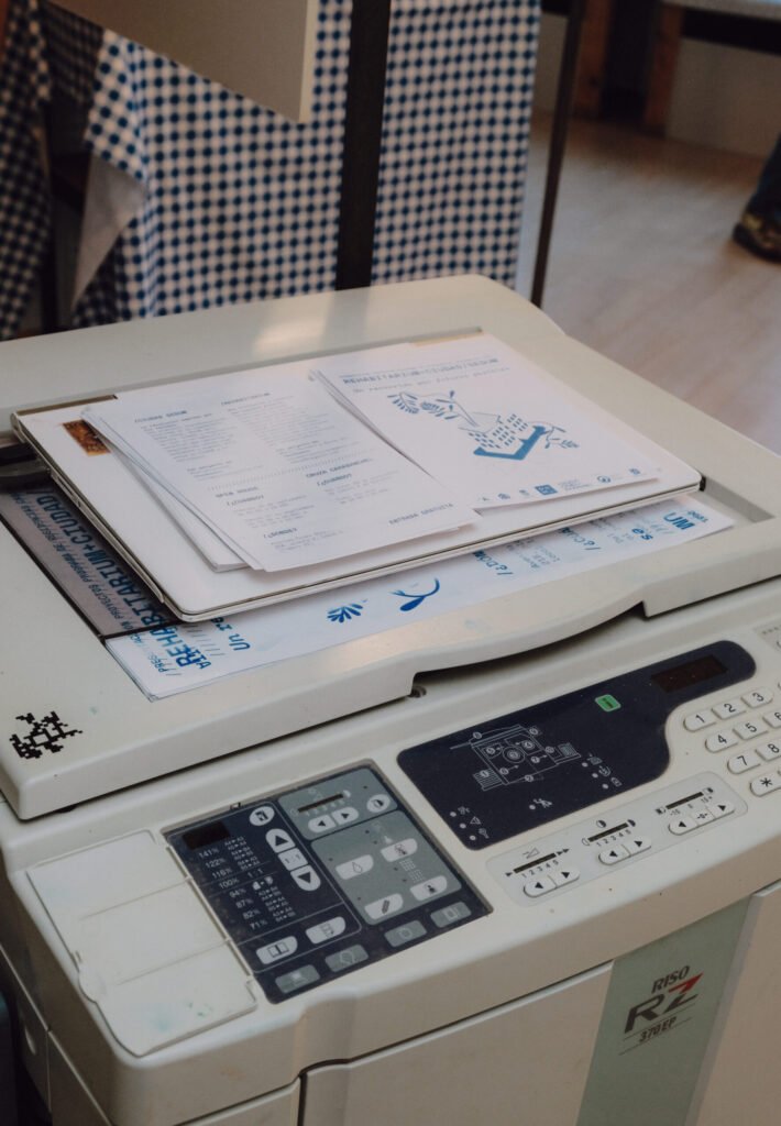 Una máquina risográfica RISO RZ con varios ejemplares del libro "Rehabitarium" y otros documentos impresos apilados sobre la tapa.