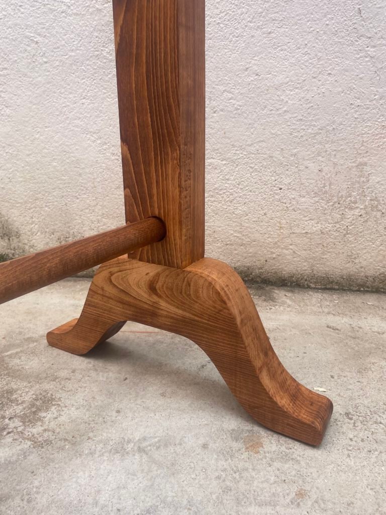 Detalle de la base del perchero de madera, mostrando la pata curva tallada que sostiene el poste vertical y el travesaño horizontal inferior.