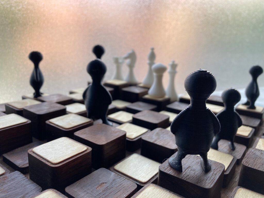 Primer plano de las piezas negras impresas en 3D con forma de figuras de pie, con las capas de impresión visibles, sobre el tablero de casillas de madera a distintas alturas.